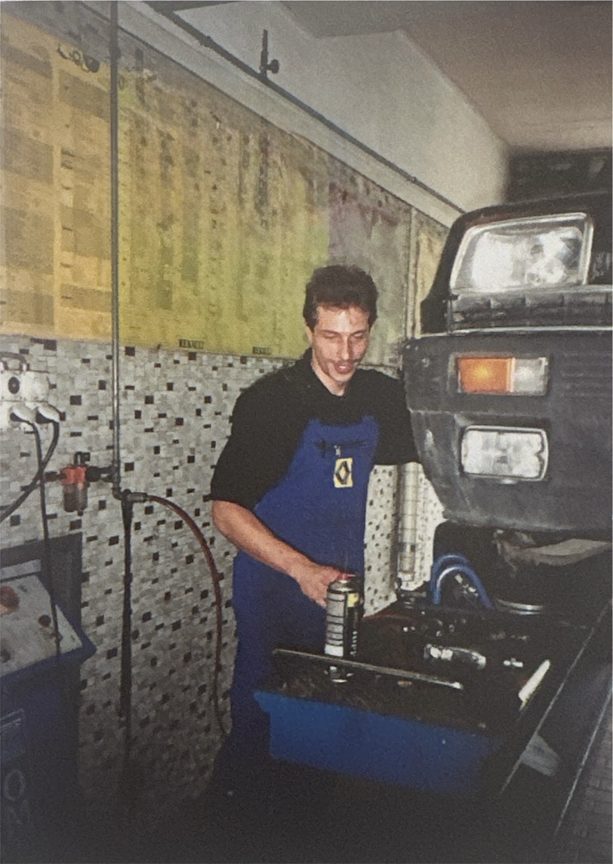 Helmut Walker als junger Mechaniker in blauer Renault-Schürze an der Front eines Fahrzeugs in der Werkstatt der Garage Walpen.