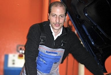 Helmut Walker als junger Automobilmechaniker in Arbeitskleidung an einem geöffneten Motorraum.