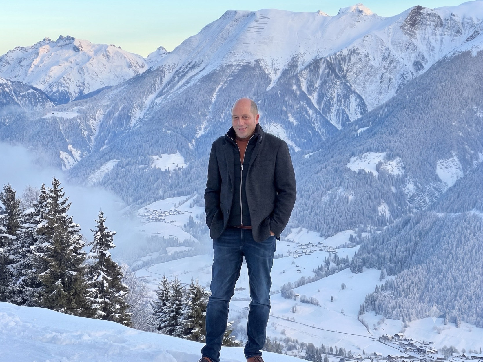 Helmut Walker steht auf einem verschneiten Grat im Oberwallis, hinter ihm das Tal und die schneebedeckten Berge.